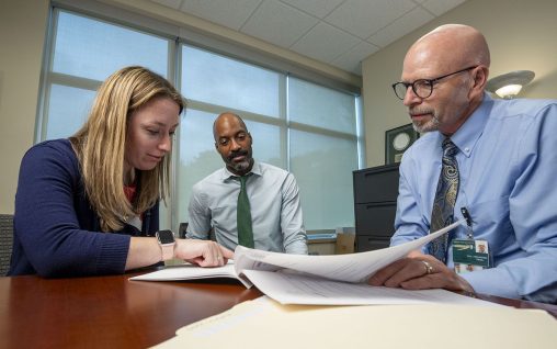 Three people in conference room reviewing paperwork