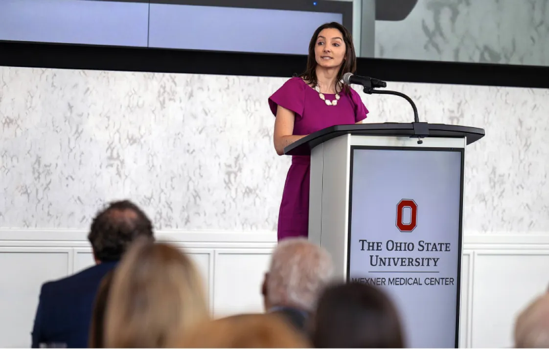 Woman standing at podium speaking to larger group